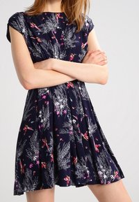 Navy dress with a floral pattern featuring birds and plants, short sleeves, pleated skirt, made of lightweight fabric.