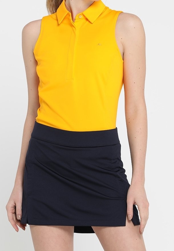 Gul ärmlös pikétröja med krage kombinerad med en marinblå skort. Piken har en diskret logga och en mjuk tygtextur.