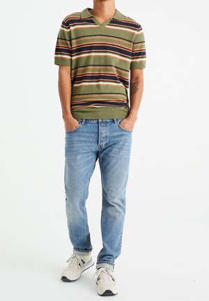 Polo a maniche corte verde a righe con strisce orizzontali multicolori, abbinato a jeans blu e sneakers beige. Taglio e design casual.