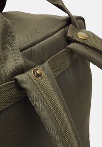 Grønn stoff ryggsekk med teksturert overflate, utstyrt med en messingknapp og sterke lerretsstropper for holdbarhet.