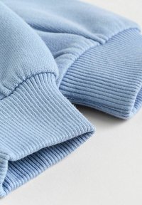 Vaaleansininen collegepaidan hihansuu esillä, joka on varustettu ribatulla tekstuurilla ja pehmeällä kankaalla. Saumassa on pieniä rypytyksiä mukavuutta varten.