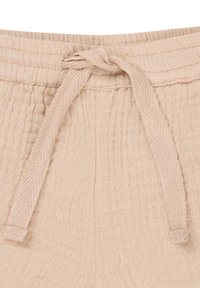 Lichtbeige katoenen broek met een trekkoord in de taille, voorzien van een geribbelde textuur en een knoopdetail aan de voorkant. De stof lijkt zacht en ademend te zijn.