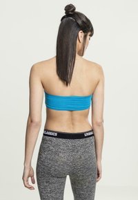 Turkise tettsydd bandeau topp kombinert med grå melange leggings som har en svart linning med "URBASICS" logo. Jevn tekstur, tett passform.