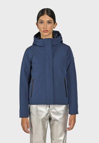 Mörkblå zip-up jacka med huva, två fickor med dragkedja på sidorna och en slät yta; matchad med blanka silverbyxor.