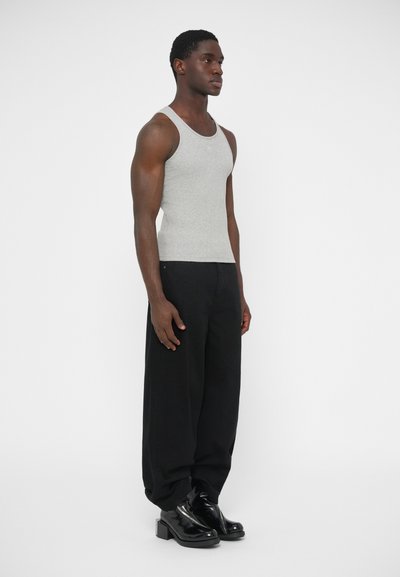 Sivý tielko z mäkkej dresovej tkaniny v kombinácii s čiernymi širokými nohavicami a lesklými čiernymi čižmami. Modelka stojí z profilu.