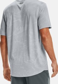 Vaaleanharmaa lyhythihainen urheilupaita, jossa on tekstuurinen, abstrakti kuvio. Sujuva kangas, pyöreä pääntie ja sivusaumat istuvuutta varten.