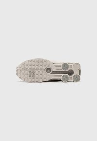 Sneaker sål i lys grå med tekstureret gummioverflade, der har cirkulære og ovale mønstre, glatte detaljer og et karakteristisk brandmotiv.