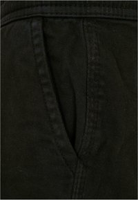 Tissu en velours côtelé noir montrant un gros plan d'une couture de poche et de la texture avec des nervures verticales et un détail de surfilage contrastant.