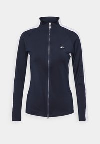 Námořnicky modrý sportovní kabát z elastické látky s vysokým límcem, celým zipem a bílými bočními pruhy. Na hrudi má malé logo.