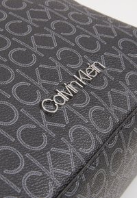 Czarna skórzana torba Calvin Klein z wytłoczonym wzorem logo, metaliczną srebrną nazwą marki i szczegółami o fakturowanej powierzchni.