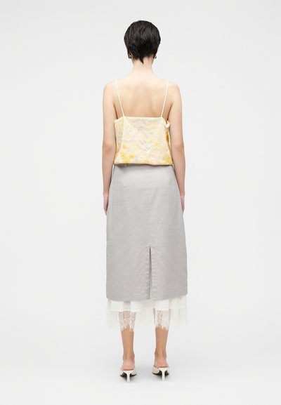 Κίτρινο κεντητό τοπ με λεπτές τιράντες, συνδυασμένο με γκρι μίντι φούστα με σχίσιμο στο πίσω μέρος, με στρώσεις από λευκή δαντέλα.