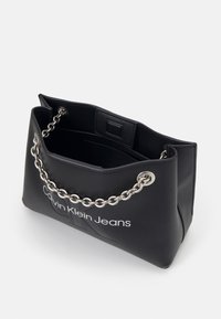 Czarna torba syntetyczna z srebrnym łańcuchem, z logo na przedzie i przestronnym wnętrzem o gładkiej teksturze.