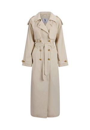 Beige lang trenchcoat med dobbeltradede knapper, midjebelte, skulderklaffer og mansjettstropper på ensfarget bakgrunn.