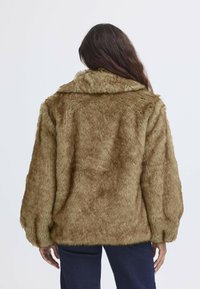 Giacca in pelliccia sintetica di colore marrone chiaro con un ampio colletto, vestibilità rilassata e maniche voluminose, caratterizzata da una superficie morbida e testurizzata.