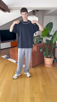 Navy blue cotton t-shirt with short sleeves, held by a person; paired with light gray vertical striped pants and white sneakers.