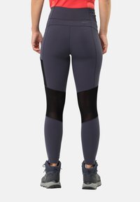Leggings de sport taille haute en gris foncé avec des inserts en maille noire. Présentent une texture lisse et un design cintré, associés à des chaussures de randonnée grises.