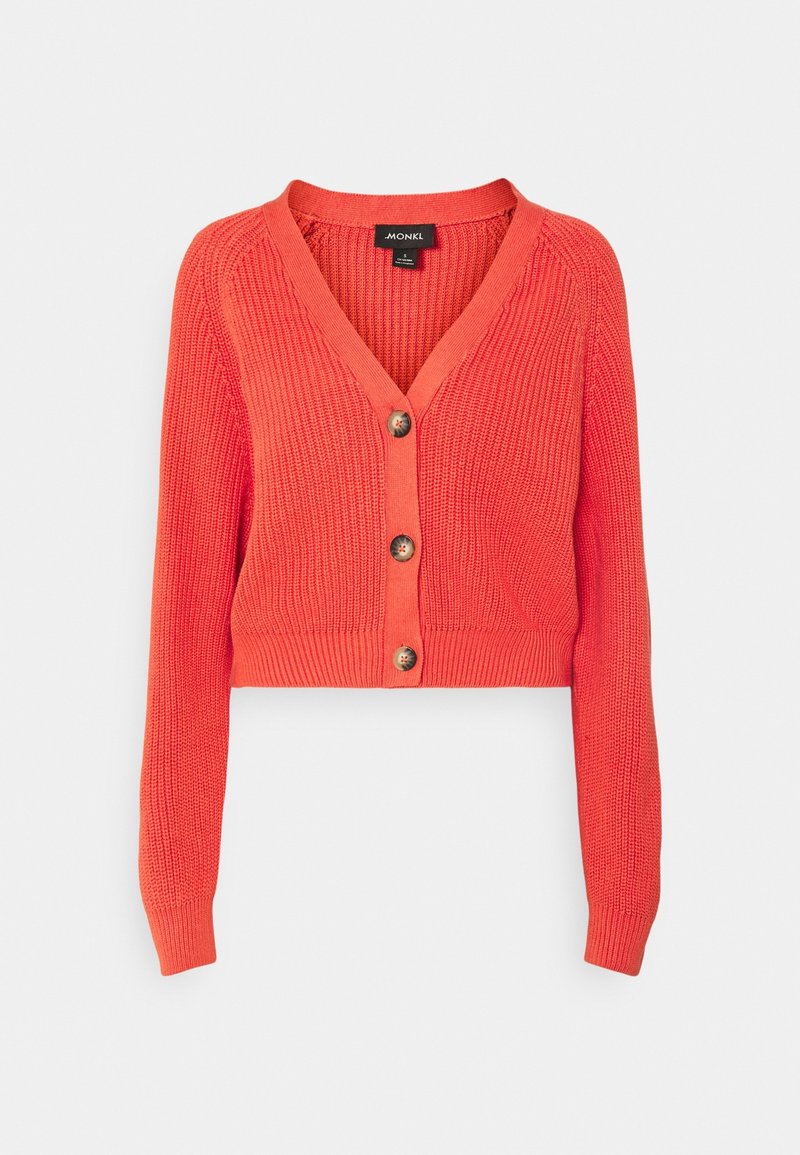 Korallfärgad kort cardigan med långa ärmar, V-ringning, ribbad struktur och fem knappar framtill. Tillverkad av ett mjukt stickat material.