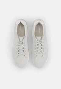 White suede sneakers with laces, rounded toe, and contrasting white rubber sole. Minimalist design with no visible branding on the exterior.