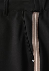 Pantalons de sport noirs avec une texture lisse, présentant une bande latérale en marron clair et beige, ainsi qu'un petit accent métallique argenté.