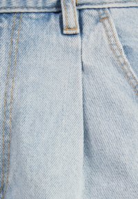 Vaaleansininen farkkukangas, jossa on klassinen kudontakuosi. Näkyvä sauma kulkee pystysuunnassa, ja vyötärön kohdalla on oranssit ompeleet.