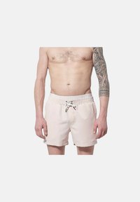 Shorts de bain rose clair avec taille élastique, fermeture à cordon, poches latérales et texture de tissu lisse. Présente un tatouage sur le bras gauche.