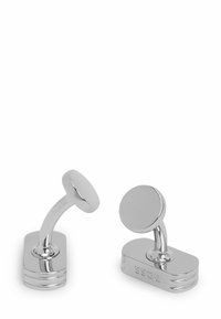 Srebrne spinki do mankietów o zaokrąglonej, przypominającej lustro powierzchni na zakrzywionej nóżce, z prostokątną podstawą zdobioną grawerowanymi akcentami.