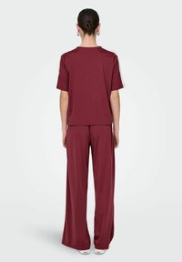 Bordeauxfarbenes Zweiteiler-Outfit mit einem locker sitzenden Kurzarm-Oberteil und einer weiten Hose, hergestellt aus weichem, dehnbarem Stoff mit minimaler Detailgestaltung.