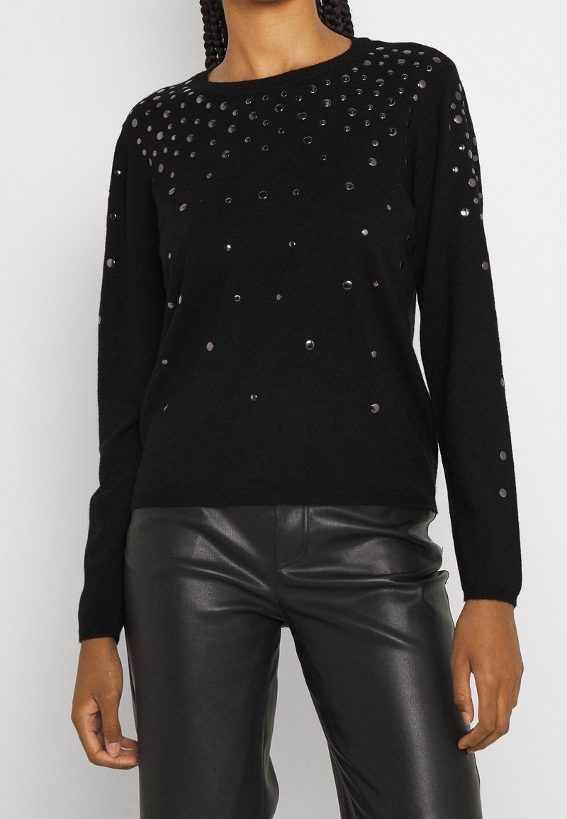 Maglione nero con paillettes tonde sul petto, maniche lunghe, scollo a giro, realizzato in tessuto morbido. Abbinato a pantaloni in pelle nera lucida.