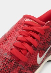 Sapatilha atlética vermelha com padrão de pele de cobra texturizado, atacadores vermelhos e o símbolo da Nike em branco na lateral.