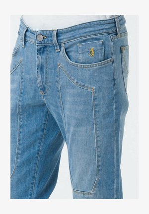 Jeans in denim blu chiaro con una vestibilità rilassata, caratterizzati da cuciture gialle, diverse tasche e un piccolo logo vicino alla tasca anteriore.