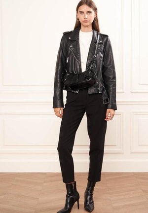 Giacca da biker in pelle nera con dettagli in acciaio inox, camicia bianca, pantaloni neri sartoriali e stivaletti con tacco. Inclusa una borsa a tracolla in vernice nera.