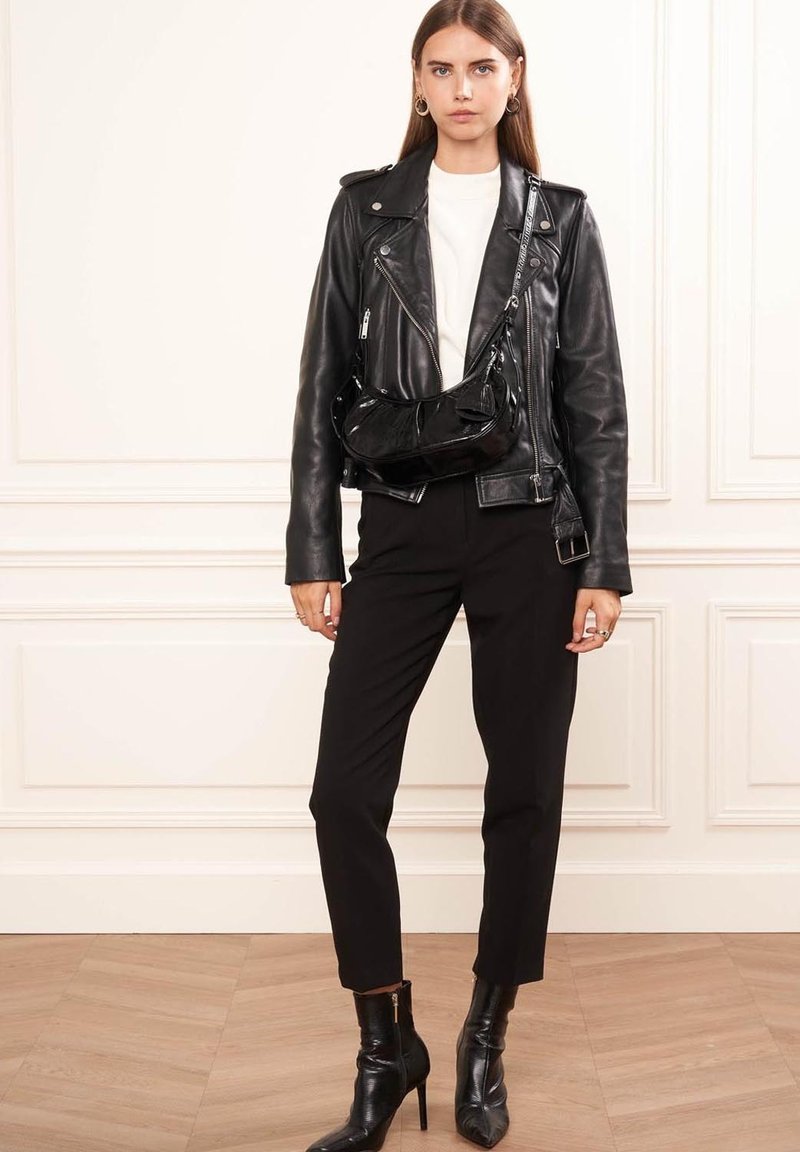 Veste de biker en cuir noir avec quincaillerie argentée, chemise blanche, pantalon noir ajusté et bottines à talons. Sac bandoulière en cuir verni noir inclus.