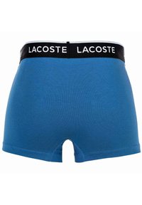 Niebieskie bawełniane bokserki z czarnym elastycznym pasem z napisem "LACOSTE". Charakteryzują się gładką fakturą i małym wycięciem z tyłu.