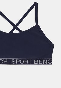 Mornarska športna modrček s prečnimi trakovi in raztegljivim pasom, ki vsebuje besedilo "SPORT BENCH" v svetlo sivi barvi. Gladka tekstura blaga.