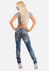 Jeans in denim blu con una finitura sbiadita e tasche posteriori decorative. Abbinati a un top corto grigio e scarpe con tacco.