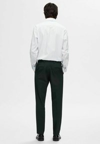 Wit gestreepte overhemd met kraag, gecombineerd met donker groene broek, gezien vanaf de achterkant, met zakken en zwarte schoenen.