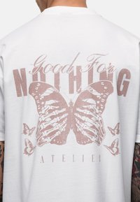 Witte katoenen t-shirt met een grote roze vlinderafbeelding op de achterkant, met de tekst "Good For NOTHING" en kleinere vlinders.