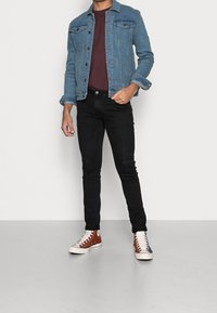 Vaaleansininen farkkutakki, jossa on napillinen kiinnitys, yhdistetty tummanpunaisen t-paitaan ja mustiin kapeisiin farkkuihin. Ruskeat ja valkoiset korkeavartiset tennarit.