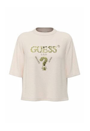 T-shirt beige a maniche corte con la scritta "GUESS U.S.A." e un disegno di un punto interrogativo con paillettes, inclusi i dettagli testuali "Washed" e "Jeans".