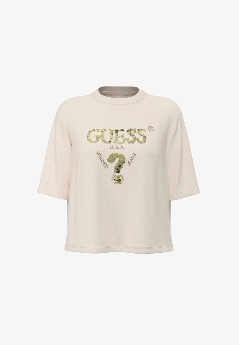 T-shirt beige à manches courtes avec le texte "GUESS U.S.A." et un motif de point d'interrogation en sequins, comprenant également les détails textuels "Washed" et "Jeans".