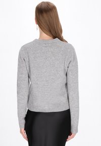 Szürke kötött pulóver hosszú ujjakkal, kerek nyakkivágással és bordás aljjal. Sima textúra, minimalista design, hátul egy kis címkével.