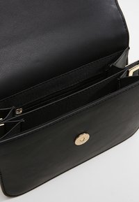 Borsa in pelle nera con una texture liscia, dotata di una chiusura con bottone color oro e diversi scomparti interni, incluso un taschino con zip.