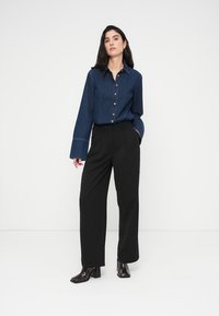 Πουκάμισο από denim με κουμπιά, γιακά, μακριά μανίκια και χαλαρή γραμμή, συνδυασμένο με ψηλόμεσα μαύρα παντελόνια με φαρδιά μπατζάκια και μπότες με τακούνι.