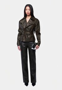 Brązowa skórzana kurtka motocyklowa z szerokimi klapami, paskiem w talii i guzikami, zestawiona z dopasowanymi skórzanymi spodniami i małą torebką.