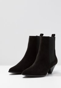 Botines de ante negros con punta afilada, tacón bajo y paneles laterales elásticos. Textura suave y diseño minimalista. Adecuados para diversos conjuntos.