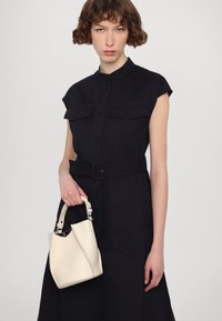 Mornarska košulja haljina s kratkim rukavima, kopčanje na gumbima i dva džepa na prsima, uparen sa krem torbom od kože koja ima struktuirani oblik.