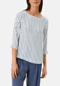 Top a righe con maniche a tre quarti, caratterizzato da strisce blu verticali su uno sfondo bianco. Tessuto morbido con taglio rilassato e orlo arrotondato.