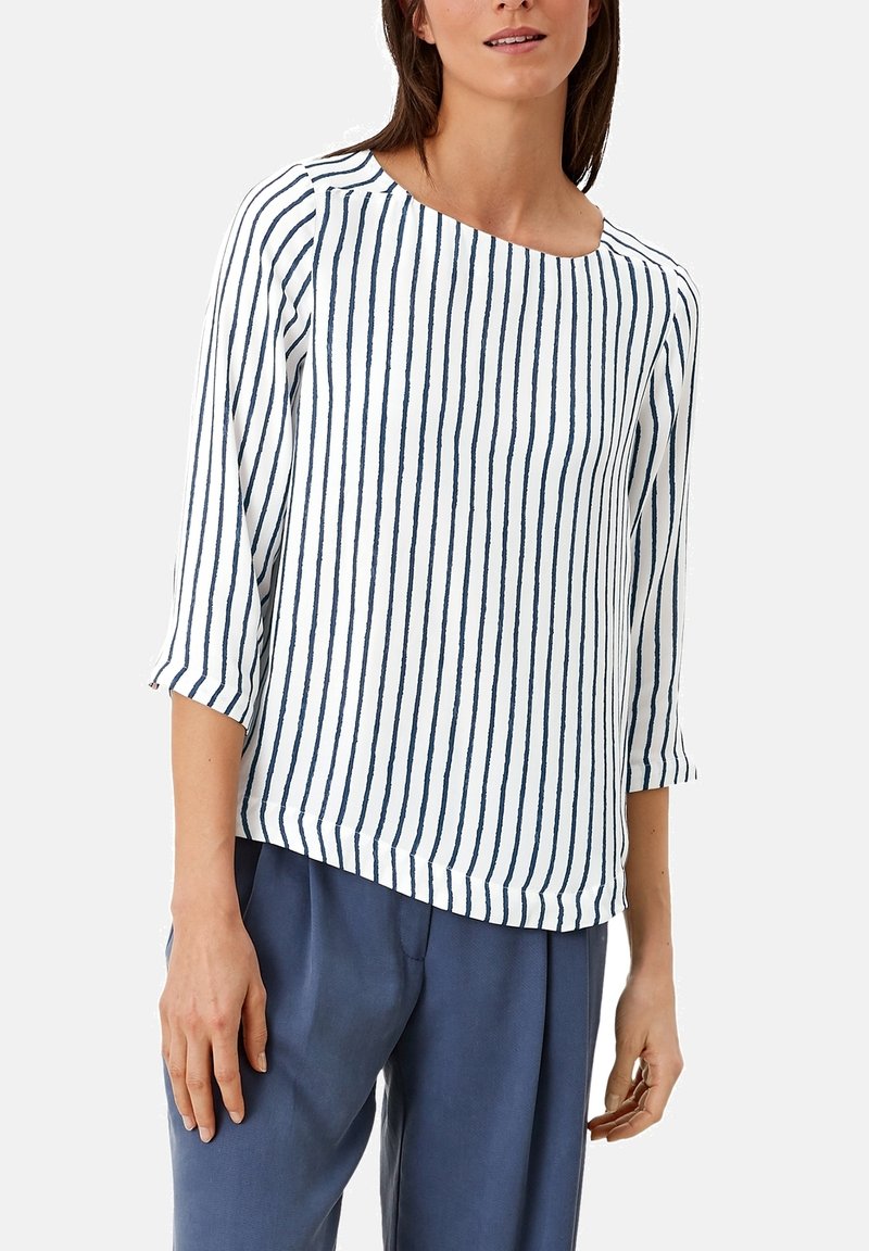 Top a righe con maniche a tre quarti, caratterizzato da strisce blu verticali su uno sfondo bianco. Tessuto morbido con taglio rilassato e orlo arrotondato.