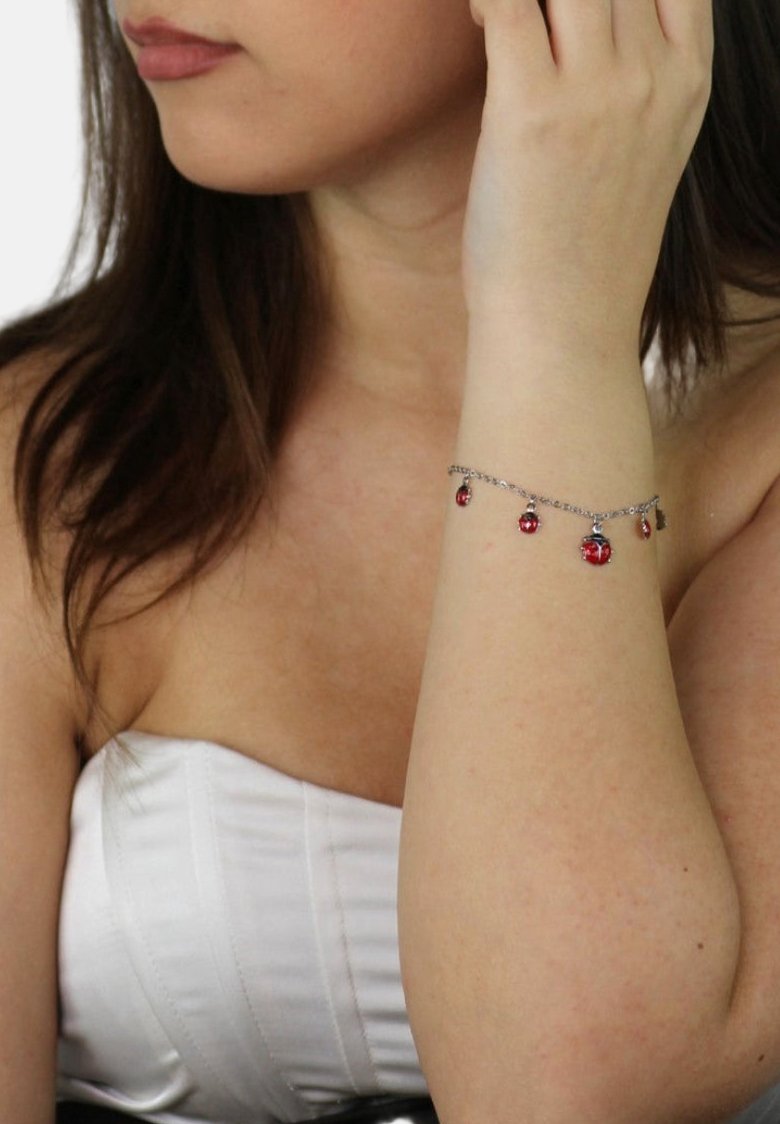Bracciale d'argento con ciondoli rossi circolari, caratterizzato da una delicate catena. Il modello indossa un top bianco senza spalline, evidenziando l'accessorio sul suo polso.