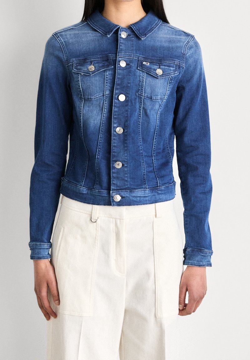 Blå denimjacka med figurnära design, två bröstfickor och silverknappar. Den har en klassisk krage och är kort i midjan.